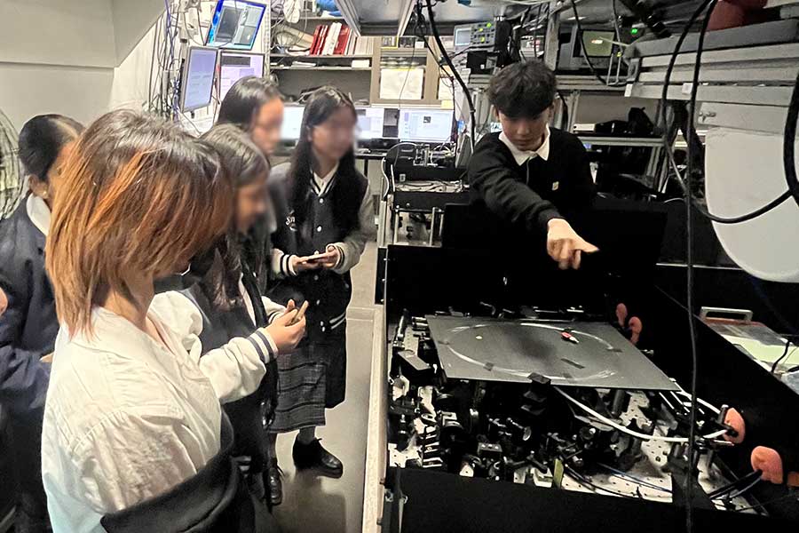 Honours student, Grant Chan, points out a high-power laser system that is enclosed to maintain stability, prevent interference, and ensure safety during experiments