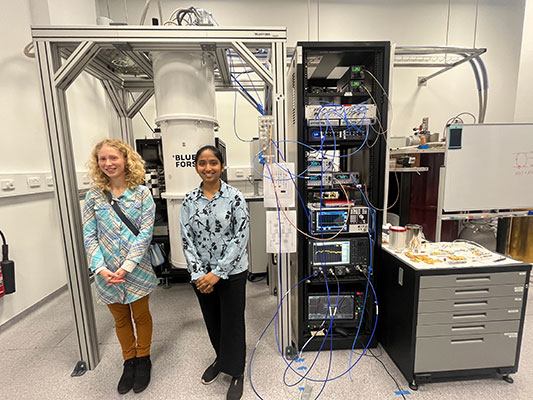 Honours students Aruna Sathyanarayanan Balaprabhavathi and Michelle Kazarinov next to the dilution fridge and microwave electronics rack.