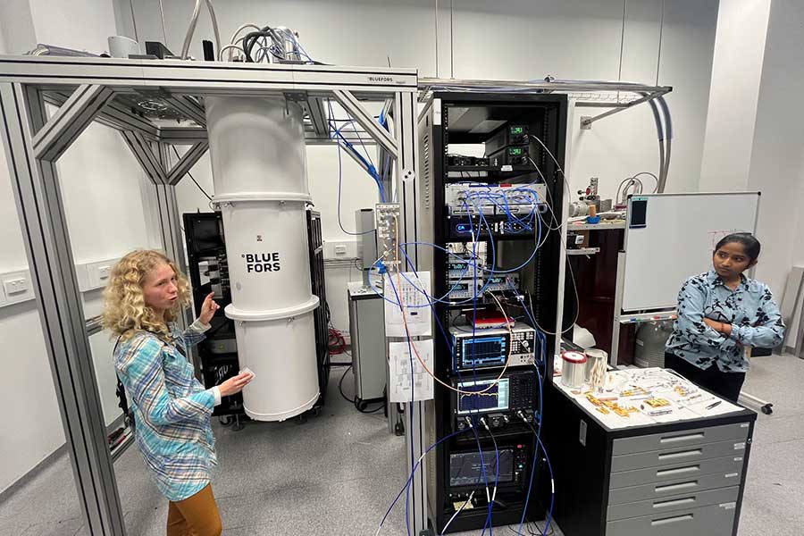 Honours student Michelle Kazarinov gesturing towards the dilution fridge in the Superconducting Quantum Circuits Laboratory