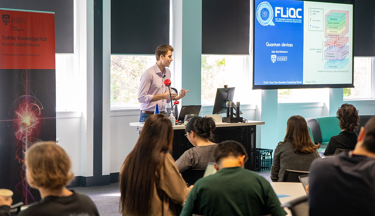 A photo of A/Prof John Bartholomew standing at a lectern and addressing a group of students at FLiQC's Quantum Computing School
